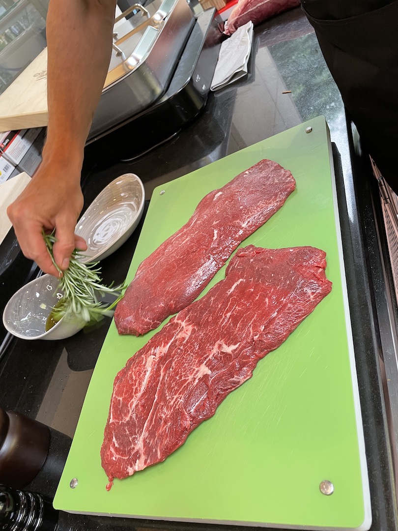Der Fleischermeister verwendet ein Büschel Rosmarin als Pinsel und bestreicht damit das Fleisch mit Öl.